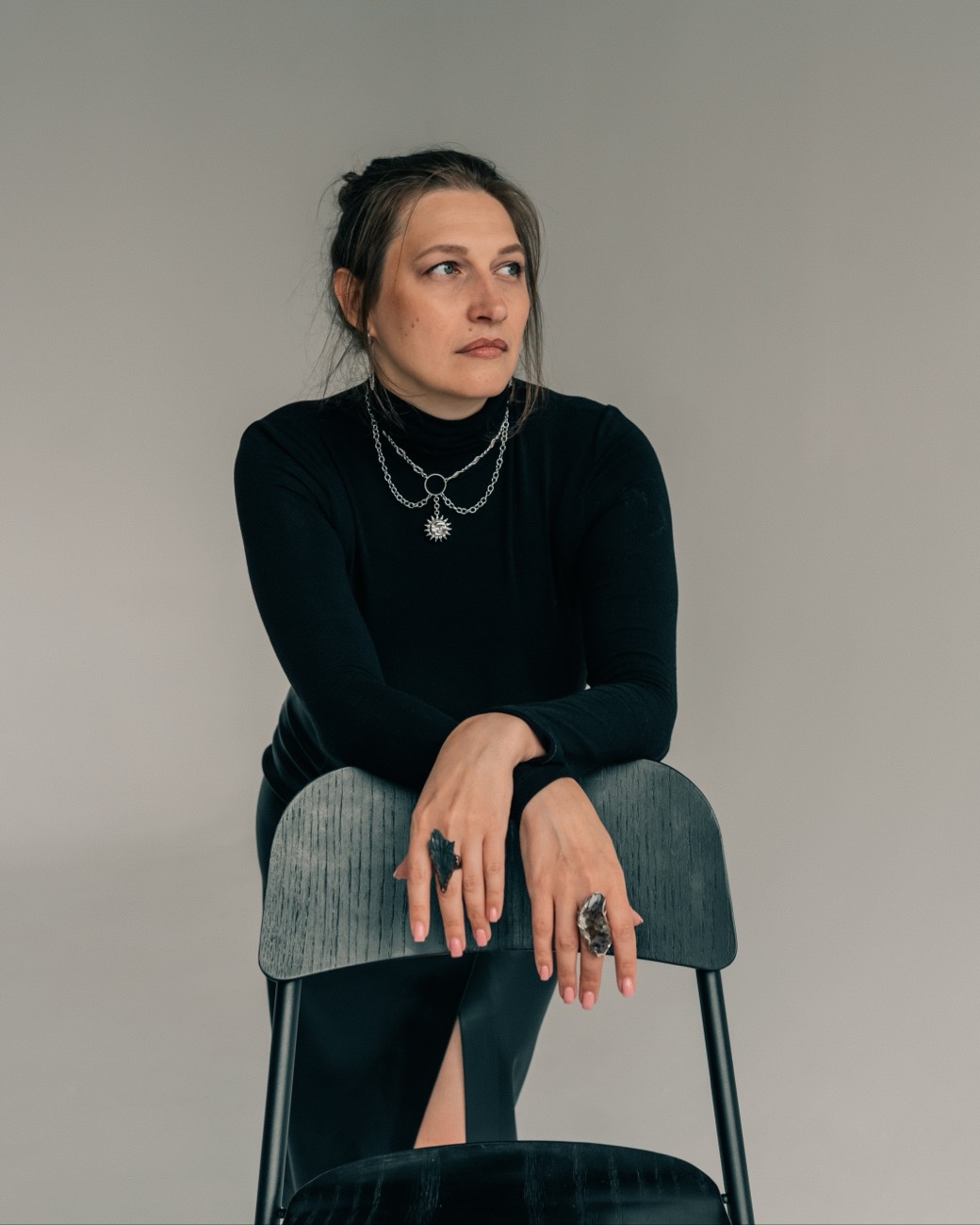 Елена Ревнивцева стоит, опершись руками на спинку стула, и задумчиво смотрит в сторону